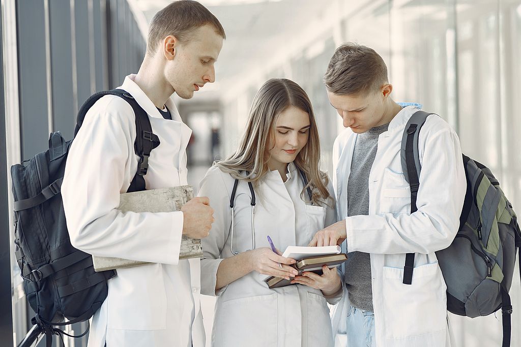 Symbolbild Ausbildung: drei junge Pflegeazubis schauen in ein Notizbuch, Link zur Seite "Informationen für Ausbildungsstätten für Pflegeberufe"