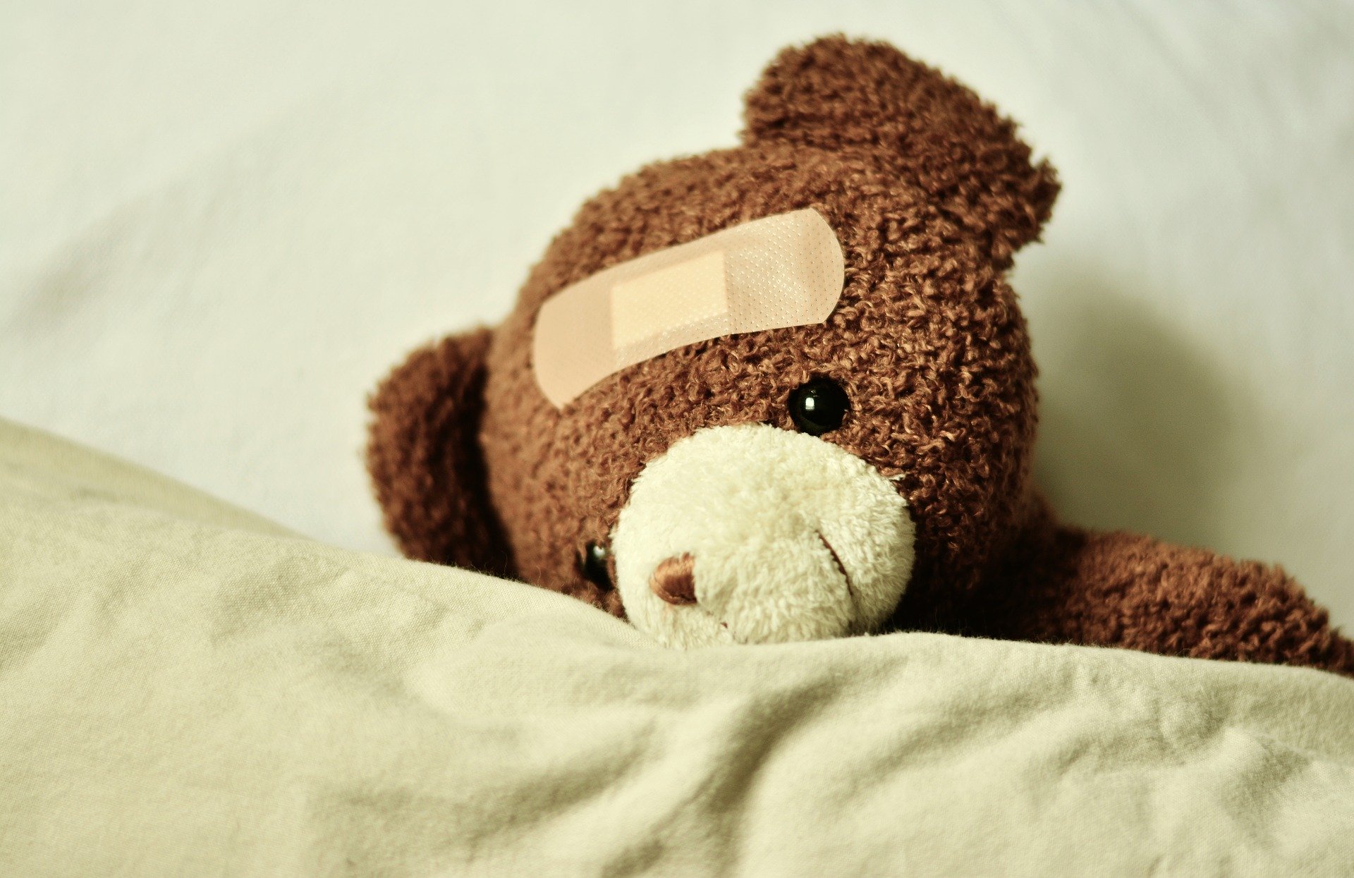 Symbolbild: Teddy mit Pflaster am Kopf, Link zur Seite "Kinder- und Jugensgesundheit"