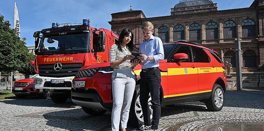 Eine Anwärterin und ein anwärter vor einem Katastrophenschutzfahrzeug