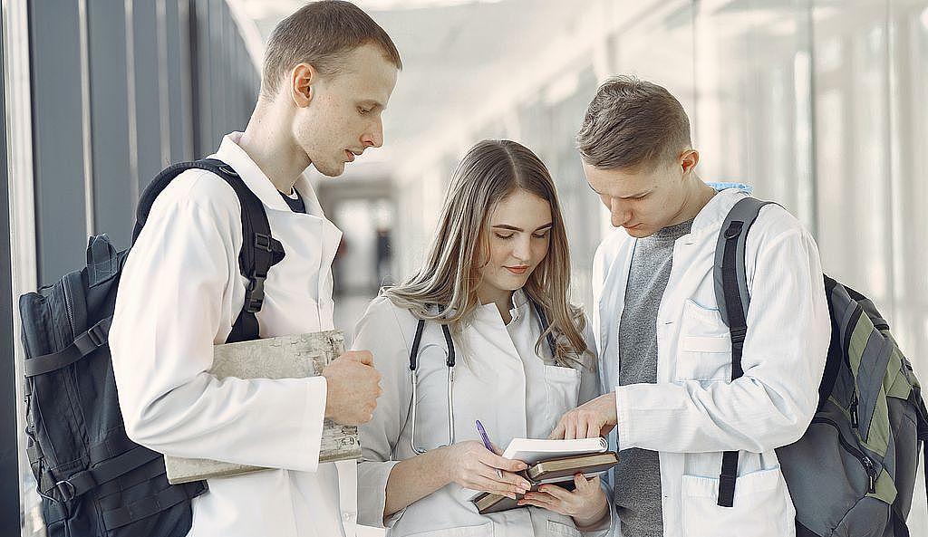 Symbolbild Ausbildung Gesundheitsberufe: drei junge Azubis schauen auf ein Notizbuch